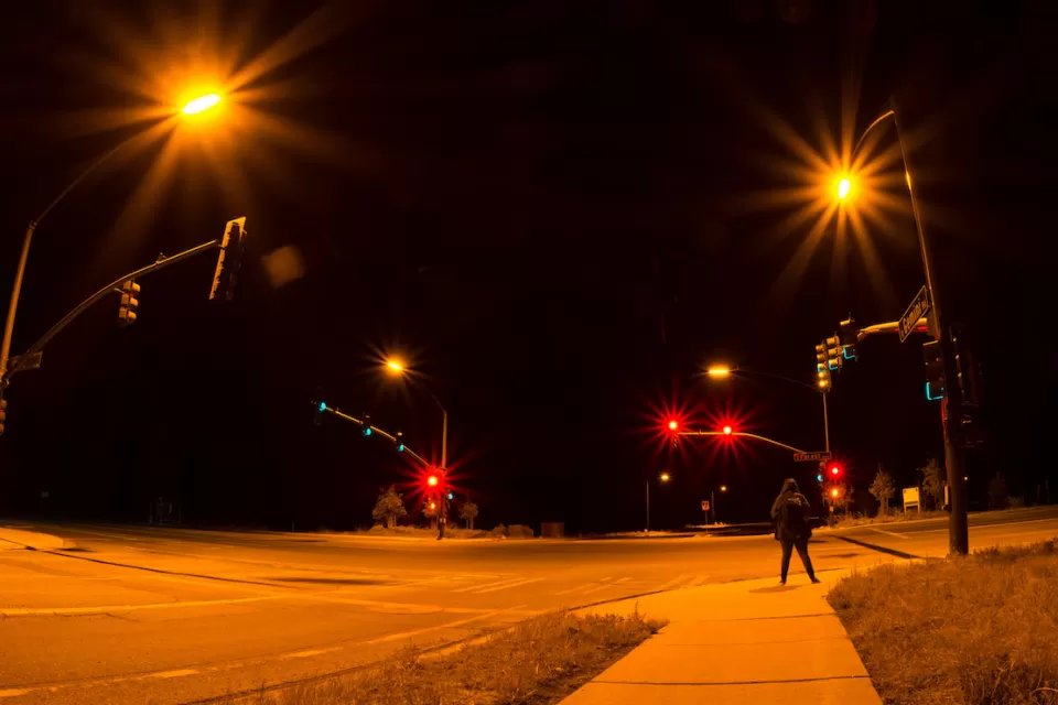 Intersection with stoplights at night with one pedestrian waiting to cross.